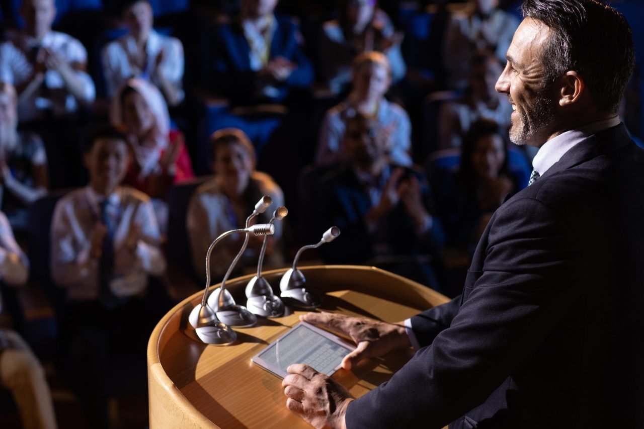 Side view of Caucasian businessman standing and giving presentation in the auditorium
