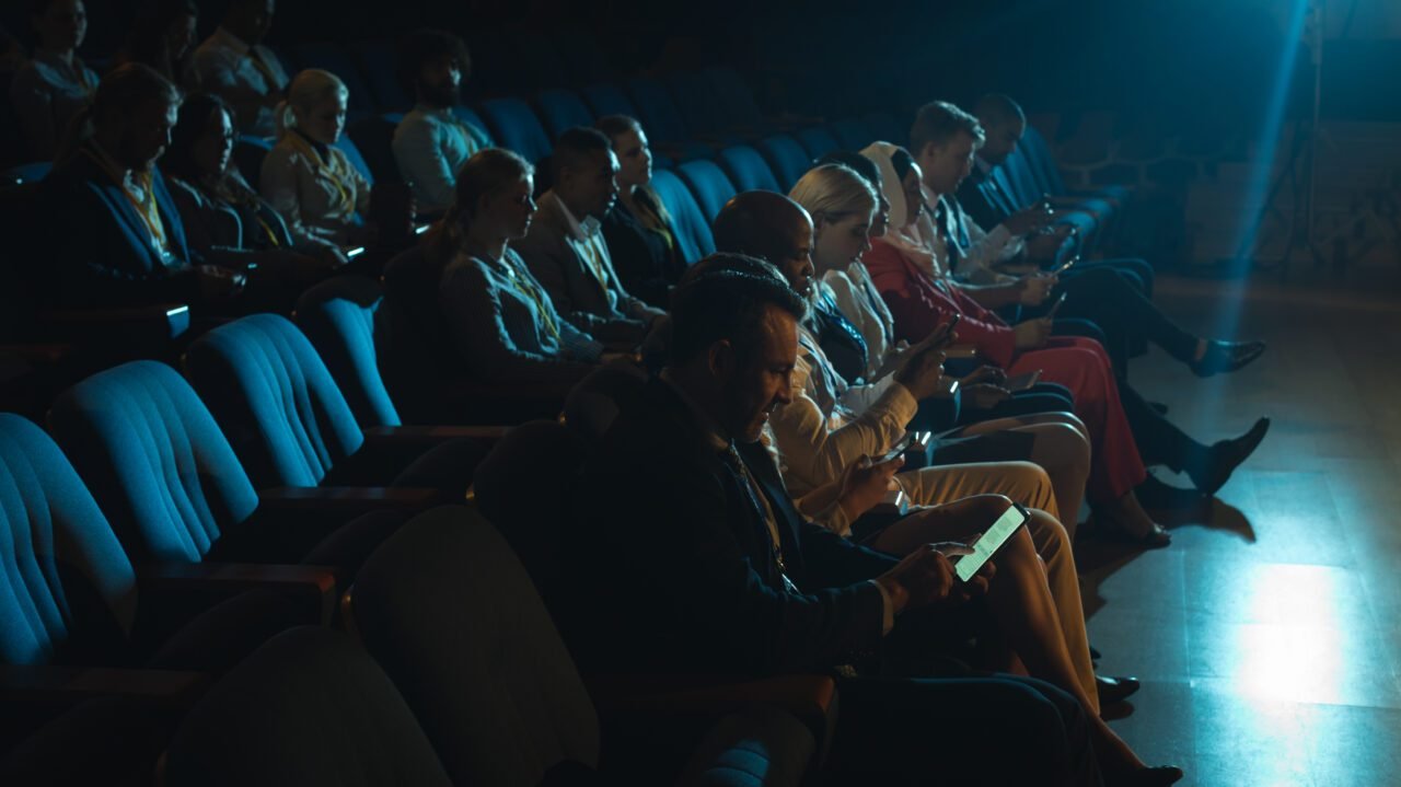 Side view of mixed race audience sitting in the auditorium and holding smartphone in their hands
