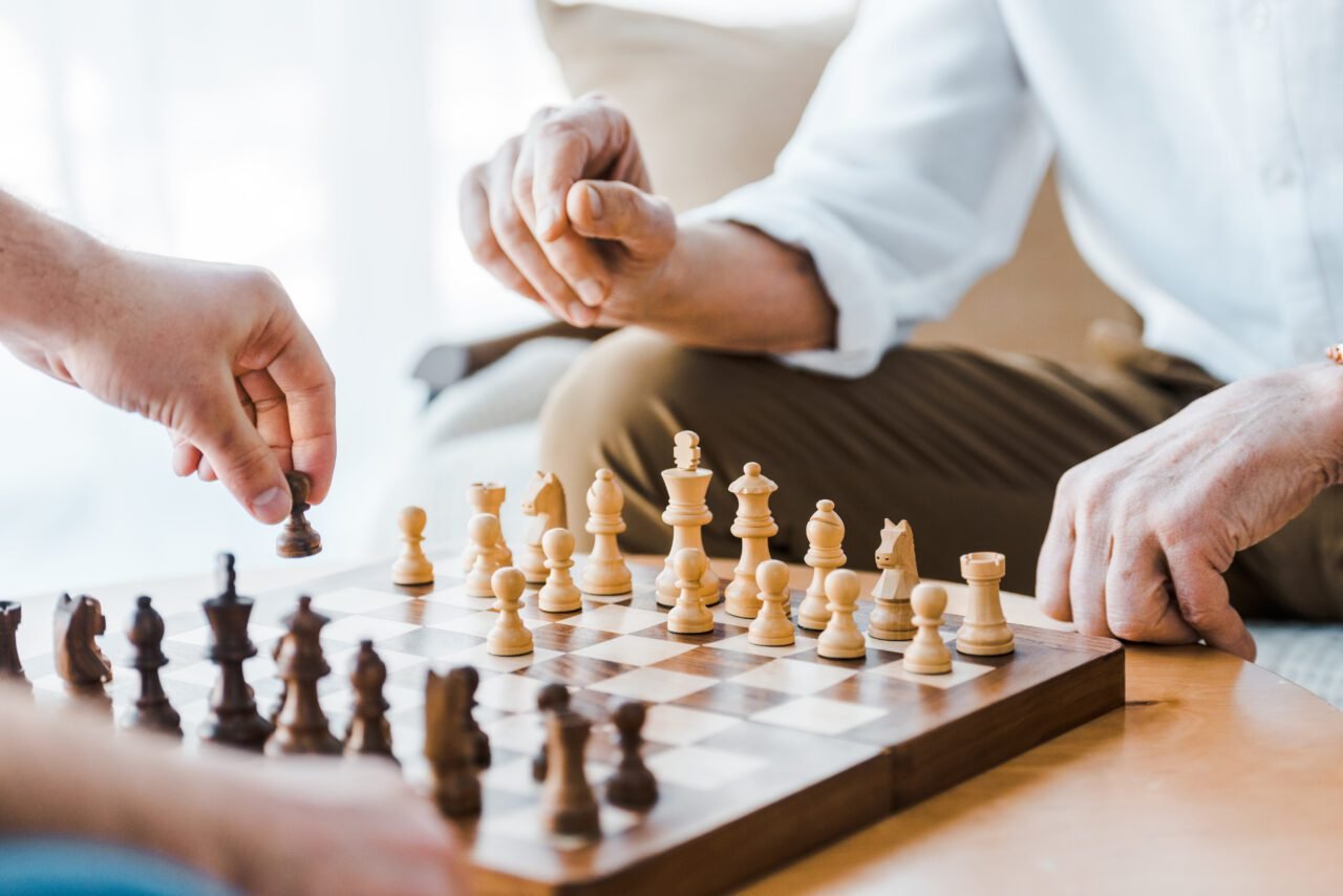 selective focus of wooden chess board with seniors playing chess at home