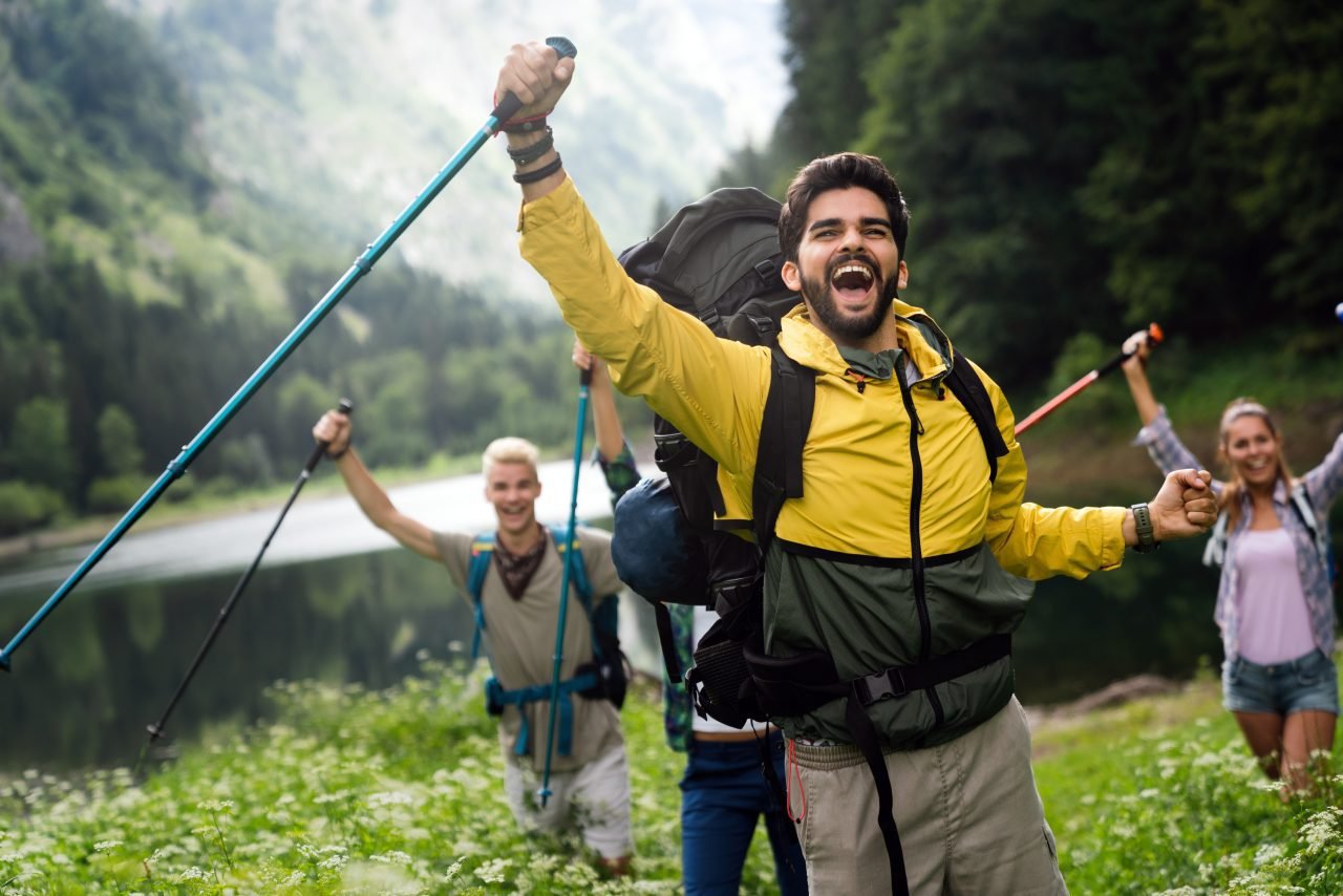 Group of smiling friends hiking with backpacks outdoors. Travel, tourism, hike and people concept.
