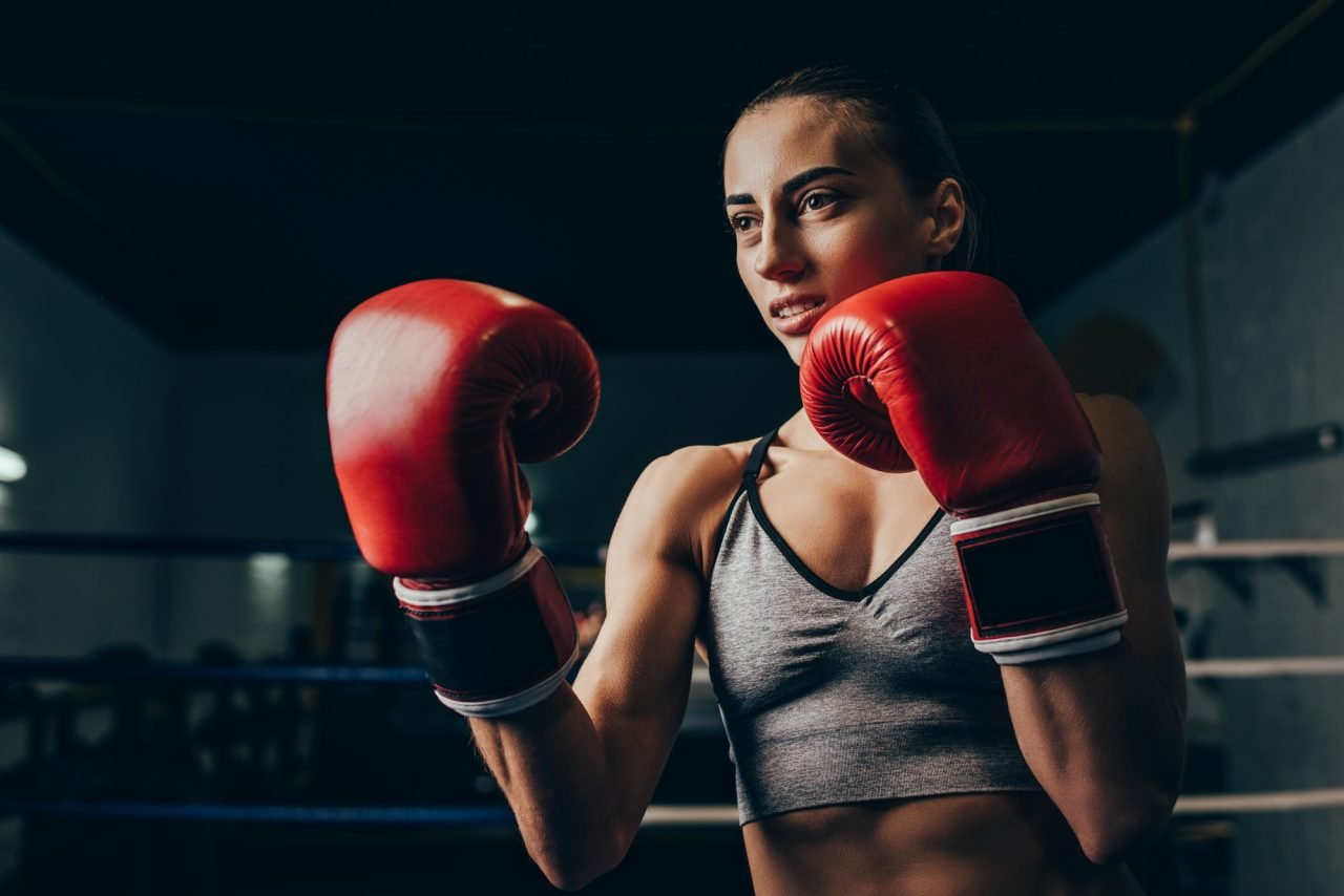 young sportswoman in boxing gloves training on boxing ring