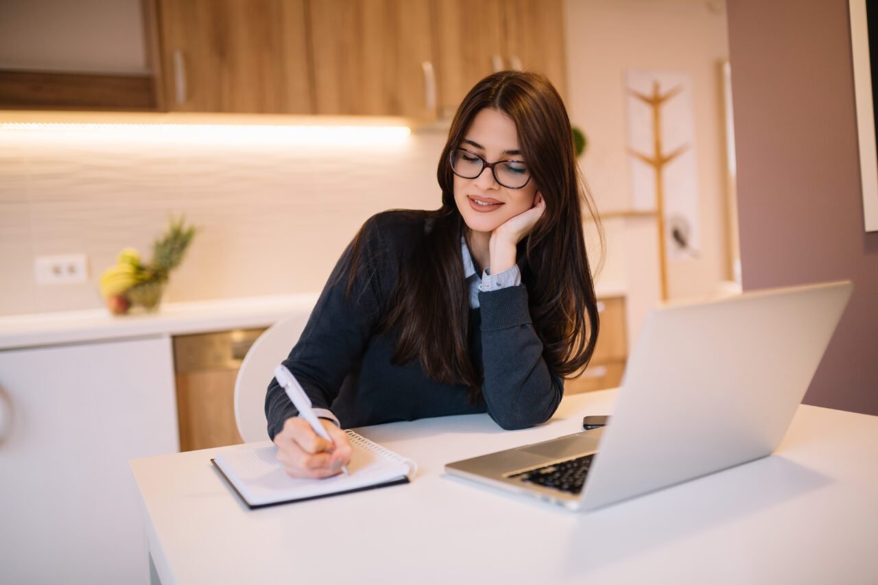 Beautiful writer with eyeglasses using laptop computer and writing her notes.
